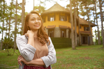Portrait of smiling Asian woman posing in front yard of her countryside house in sunlight