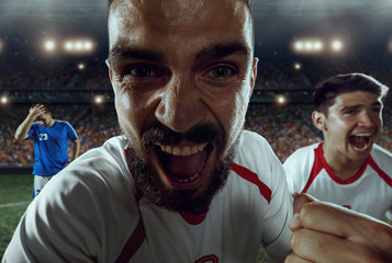 Soccer players emotionally happy after victory. Players joyfully screaming on the big professional stadium. Football team wears unbranded uniform. © Alex