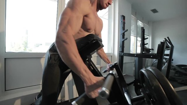 Bodybuilder trains in the gym, he works on the machine.