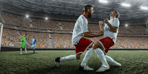 Obraz premium Soccer players emotionally happy after victory. Players joyfully screaming on the big professional stadium. Football team wears unbranded uniform.