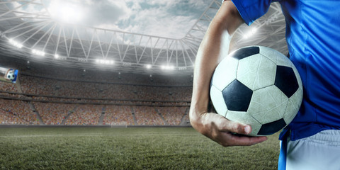 Fototapeta premium Soccer player holds a football ball on a professional stadium. Player wears blue unbranded uniform.