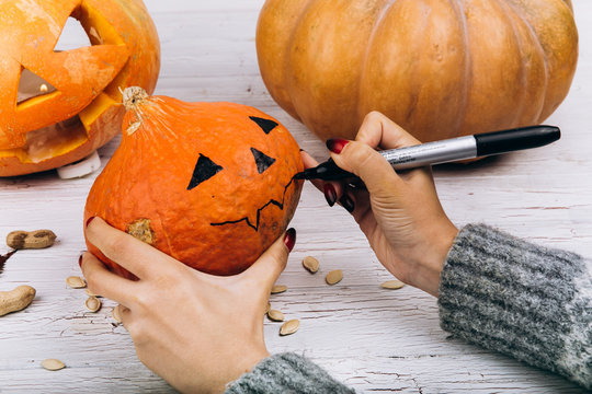 Woman paints a face on a little orange pumpkin for Halloween