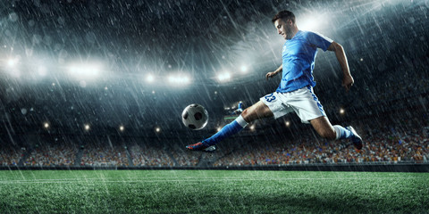 Fototapeta na wymiar Soccer player performs an action play and beats the ball on a professional rainy stadium. Player wears unbranded sport uniform.