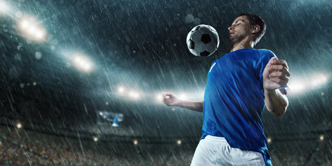 Soccer player performs an action play and beats the ball on a professional rainy stadium. Player wears unbranded sport uniform.