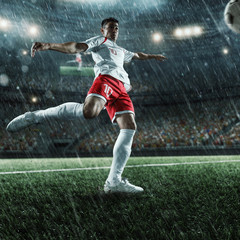 Naklejka premium Soccer player performs an action play and beats the ball on a professional rainy stadium. Player wears unbranded sport uniform.