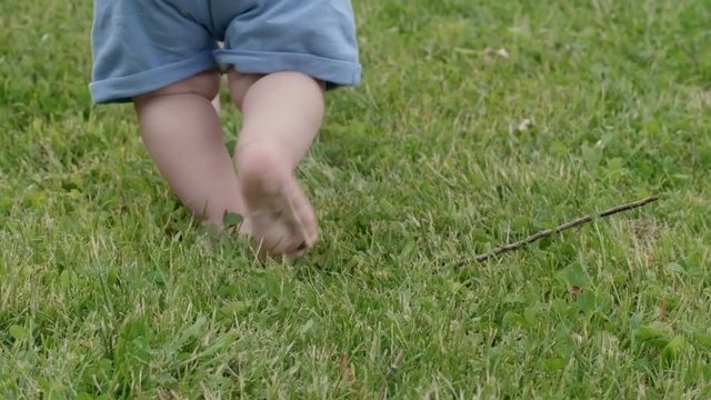 Tilt up of unrecognizable mother holding hands of little baby boy learning to walk on green grass in park with lake