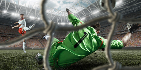 Fototapeta na wymiar Soccer player scores the ball into the goal on professional stadium. The goalkeeper protects the football gate. Players wears unbranded sport uniform. View through the football gate.