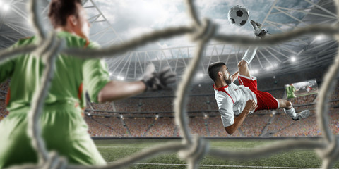 Soccer player scores the ball into the goal on professional stadium. The goalkeeper protects the...