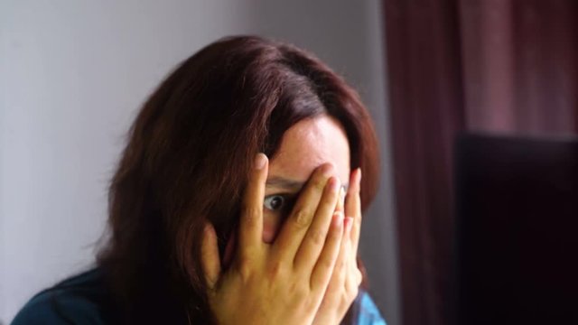 natural beauty brunette woman in front of computer watching scary movie, hide in fingers, affraid expression