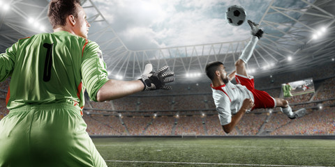 Obraz premium Soccer player scores the ball into the goal on professional stadium. The goalkeeper protects the football gate. Players wears unbranded sport uniform.