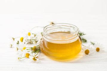 Honey in a jar with chamomile flowers on a white table