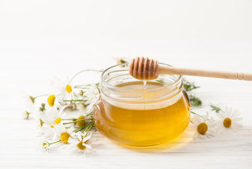 The current honey with chamomile flowers on a white table
