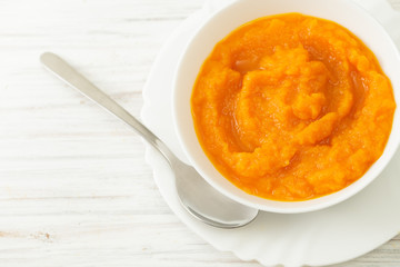 Pumpkin puree in a bowl with spoon on a white table