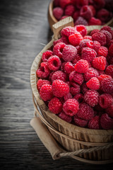 Bowl and bucket with ripe raspberries on wooden board