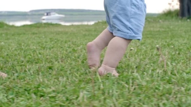 Tracking with low-section of unrecognizable woman teaching toddler boy to walk in park