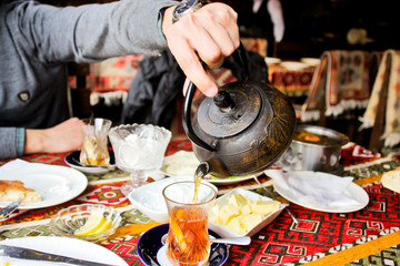 Fototapeta na wymiar A man's hand pours tea from a metal kettle. Atmosphere of Baku and Eastern traditions. Oriental cuisine. Cozy atmosphere in the caucasus cafe. The cheese and butter on a color tablecloth.