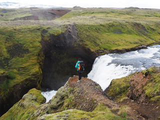 A girl with a backpack stands over a canyon with a waterfall
