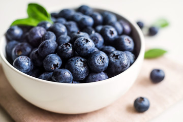 Juicy and fresh blueberries with green leaves on white bowl. Healthy eating
