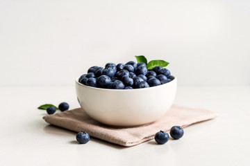 Juicy and fresh blueberries with green leaves on white bowl. Healthy eating