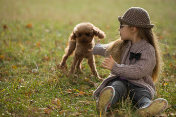 Little girl playing with dog sitting on a grass in autumn clothes