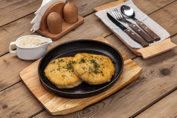 simple dish of Russian, Belarusian, Ukrainian cuisine on a old wooden boards, Potato pancakes in a frying pan on a table with sauce and cutlery
