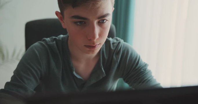 A serious teenager is sitting using a laptop in the home room. close-up, attentive, serious, homework, frustrated, surprised, tired, school, modern technology, concentrated, touches hair. Thinks