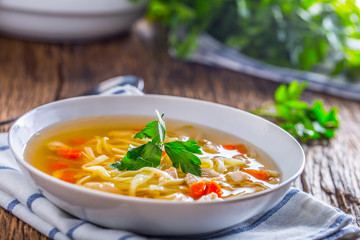 Chicken broth. Bone broth with noodles carrot and parsley in white bowl