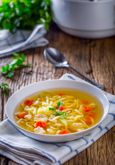 Chicken broth. Bone broth with noodles carrot and parsley in white bowl