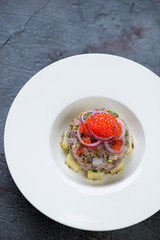 White plate with herring fillet tartare on a dark grey stone background, high angle view
