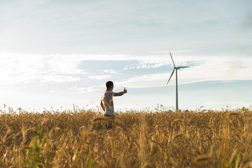 A man standing in a field looking at a wind generator
