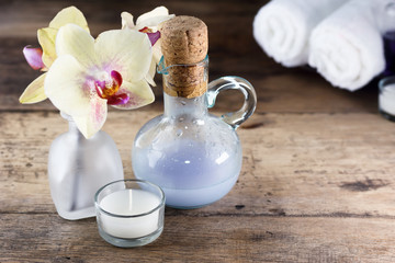 Aroma oil, orchid and candle on wooden table. Blurred massage bags and towels in background. Healthy lifestyle, spa