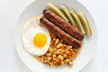 beans stewed with vegetables and herbs, fried beef sausages, pickled cucumbers, and fried egg