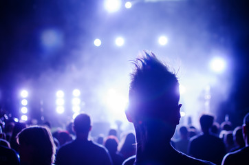 silhouettes of concert crowd and mohawk punk hair style in front of bright stage lights