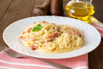 Classic pasta carbonara. Spaghetti with bacon, egg yolk and parmesan cheese on white plate on dark wooden background.