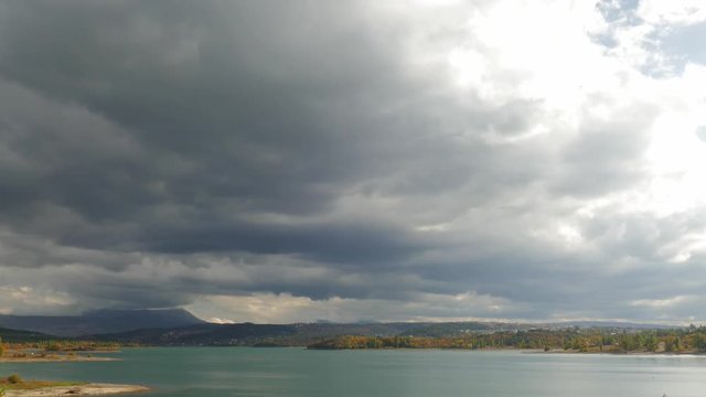 Lake and forested hills on background of sky with stormy clouds
