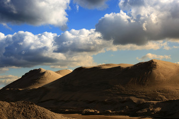 Kopalnia odkrywkowa, góra piasku na tle nieba z obłokami.