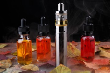 Electronic cigarette and vape liquids within vapor on wooden table with autumn leaves