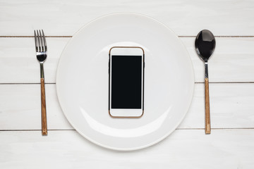 Smartphone on a white plate. View from above. On a wooden table.