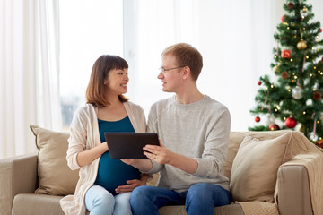 man and pregnant wife with tablet pc at christmas