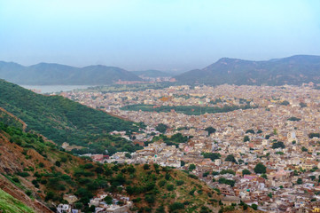 Obraz premium Cityscape of Jaipur city with the bordering Aravali hills and the city of Amber at the base. The cloudy sky and mountains in the background add to the beauty of the place