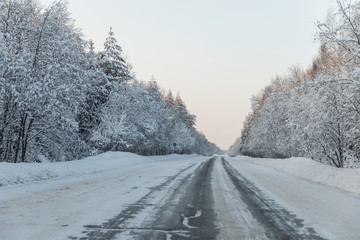 winter road with ice on the asphalt, trees under snow during the winter frost