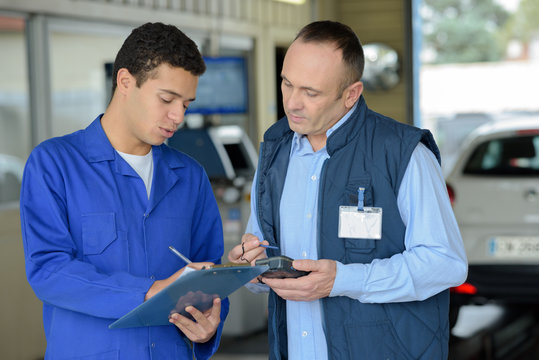 mechanic with clipboard talking to man