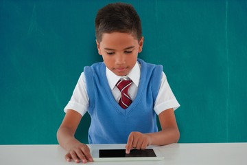 Composite image of schoolboy using digital tablet at table