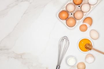 Baking cake ingredients. Milk, egg whites foam, egg beater, honey and eggshells on marble desk. Top view. Space for text.