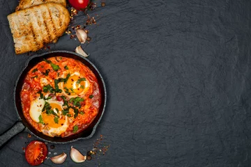 Papier Peint photo Oeufs sur le plat Breakfast. Shakshuka with bread in pan on a black rustic background. Fried eggs with tomatoes. Top view. Space for text. Middle eastern style breakfast or lunch