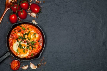 Papier Peint photo Lavable Oeufs sur le plat Breakfast. Shakshuka with bread in pan on a black rustic background. Fried eggs with tomatoes. Top view. Space for text. Middle eastern style breakfast or lunch