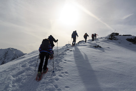 Group Of People Hiking On Snowshoes And Mountain Snow Panorama With Summit Cross In Stubai Alps, Austria