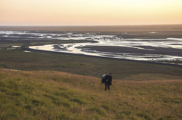 Man walking on a ledge of a mountain, enjoying the sunset over a river valley in Seljalandsfoss , Iceland. With lens flare.