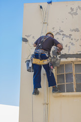 A workman hung on a facade plastering the plaster of the building.