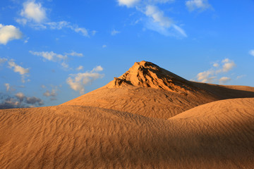 Fototapeta na wymiar Piaszczysta wydma na tle błękitnego nieba, zachód słońca.